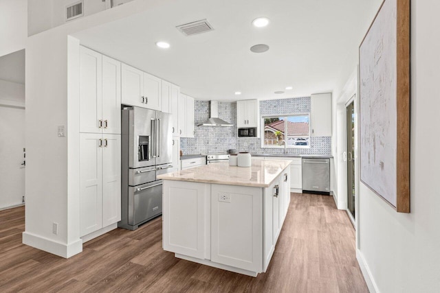 kitchen with visible vents, a kitchen island, stainless steel appliances, wall chimney range hood, and white cabinetry