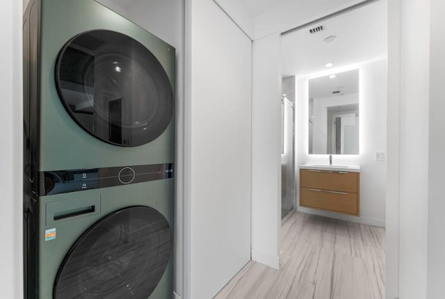 laundry area featuring laundry area, visible vents, baseboards, stacked washer / dryer, and a sink