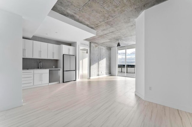 unfurnished living room with a sink, baseboards, floor to ceiling windows, and a ceiling fan