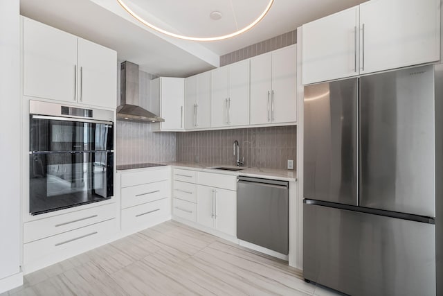 kitchen featuring stainless steel appliances, a sink, white cabinetry, light countertops, and wall chimney exhaust hood