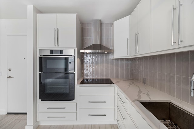 kitchen with wall chimney exhaust hood, tasteful backsplash, a sink, light stone countertops, and black appliances