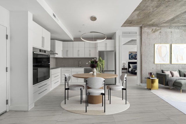 kitchen featuring decorative backsplash, multiple ovens, white cabinets, a sink, and stainless steel refrigerator