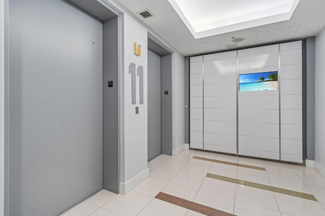 hallway featuring elevator, light tile patterned flooring, visible vents, and baseboards