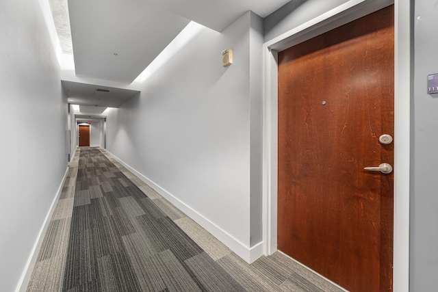 hallway featuring dark carpet and baseboards