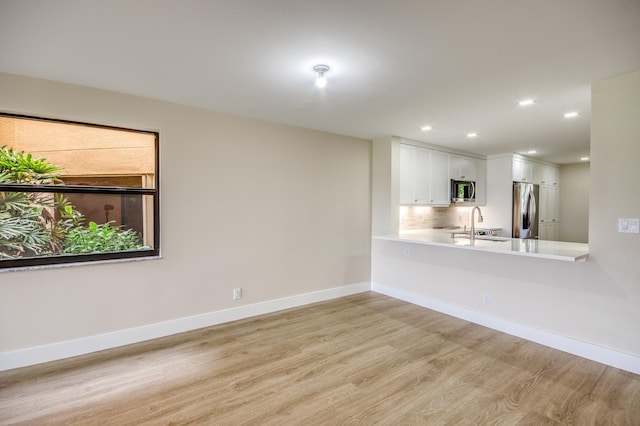 unfurnished room with light wood-type flooring, a sink, baseboards, and recessed lighting