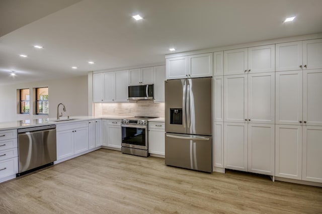 kitchen with white cabinets, stainless steel appliances, light countertops, light wood-type flooring, and a sink