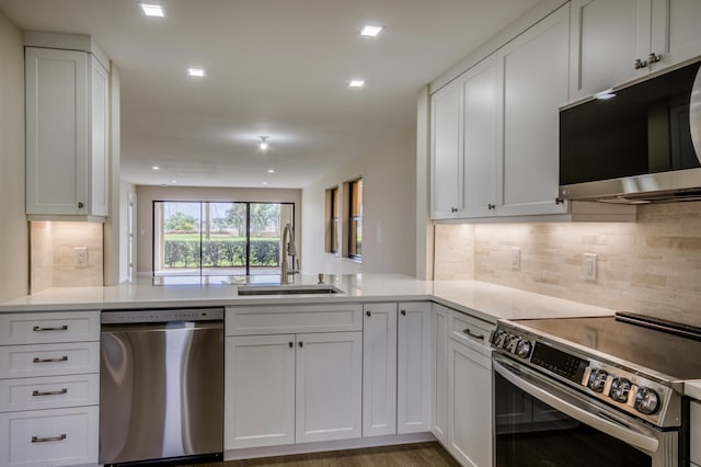 kitchen with a peninsula, a sink, white cabinets, light countertops, and appliances with stainless steel finishes