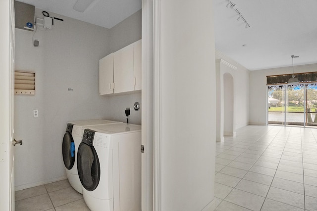 laundry area featuring arched walkways, cabinet space, light tile patterned flooring, track lighting, and washer and dryer