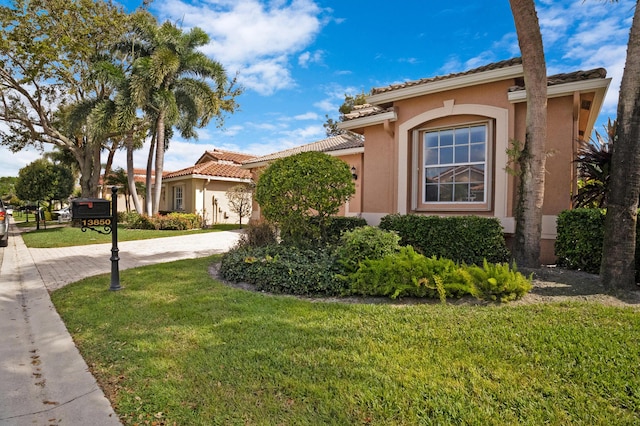 mediterranean / spanish home with driveway, a tiled roof, a front lawn, and stucco siding