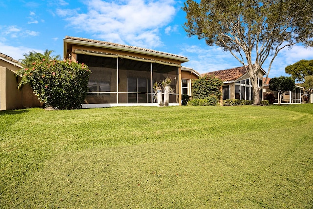 rear view of house featuring a sunroom, a lawn, and a tiled roof