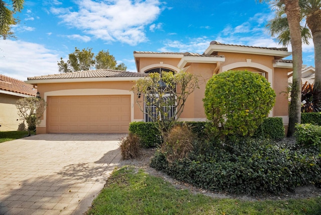 mediterranean / spanish house featuring a tiled roof, decorative driveway, an attached garage, and stucco siding