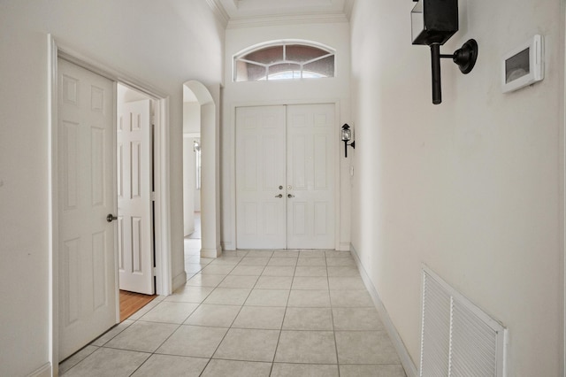 interior space featuring arched walkways, light tile patterned flooring, visible vents, baseboards, and crown molding