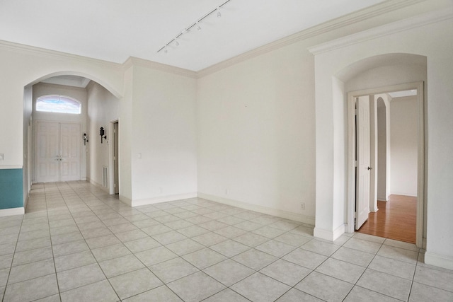 spare room featuring arched walkways, light tile patterned flooring, crown molding, baseboards, and track lighting