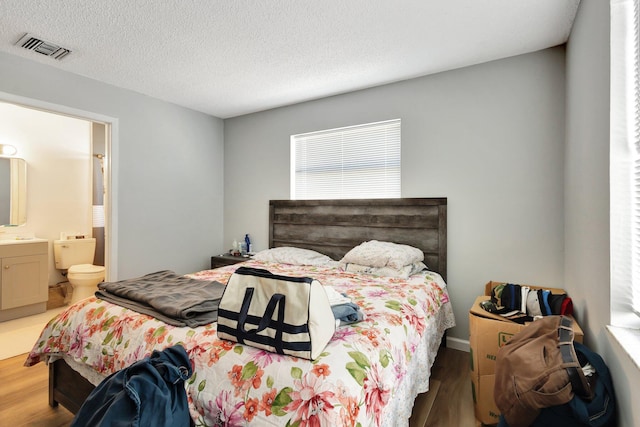 bedroom featuring a textured ceiling, wood finished floors, visible vents, and connected bathroom