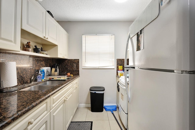 kitchen featuring freestanding refrigerator, white cabinetry, a sink, and dark stone countertops