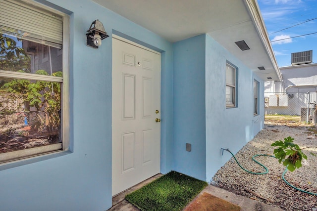 property entrance featuring central AC unit, fence, and stucco siding