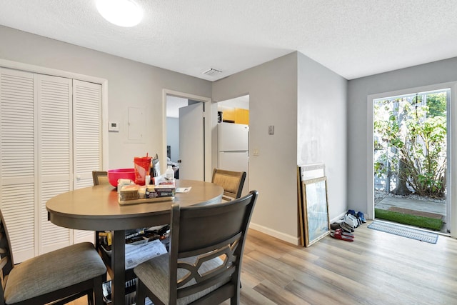 dining space with light wood-type flooring, visible vents, a textured ceiling, and baseboards