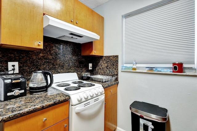 kitchen featuring under cabinet range hood, tasteful backsplash, dark stone counters, and white range with electric cooktop