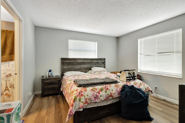 bedroom with a textured ceiling, wood finished floors, and baseboards