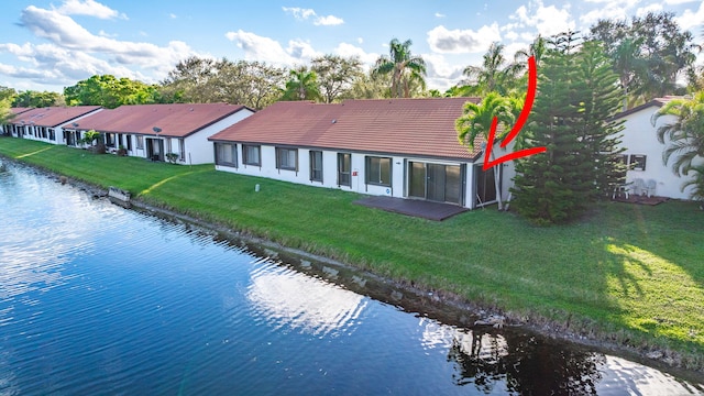 back of house with a water view, a yard, and a tiled roof