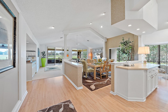 kitchen featuring light wood-style flooring, open floor plan, light countertops, vaulted ceiling, and ornate columns