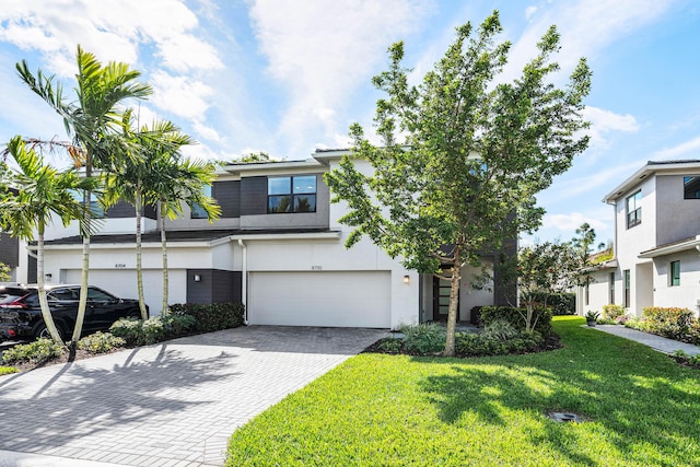 view of front of house featuring an attached garage, decorative driveway, a front yard, and stucco siding