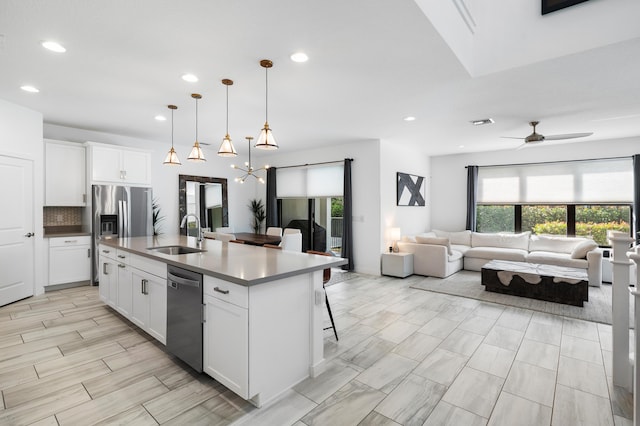 kitchen with hanging light fixtures, appliances with stainless steel finishes, open floor plan, a kitchen island with sink, and a sink