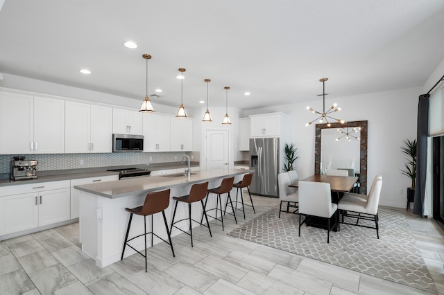 kitchen featuring a center island with sink, stainless steel appliances, hanging light fixtures, white cabinetry, and a sink