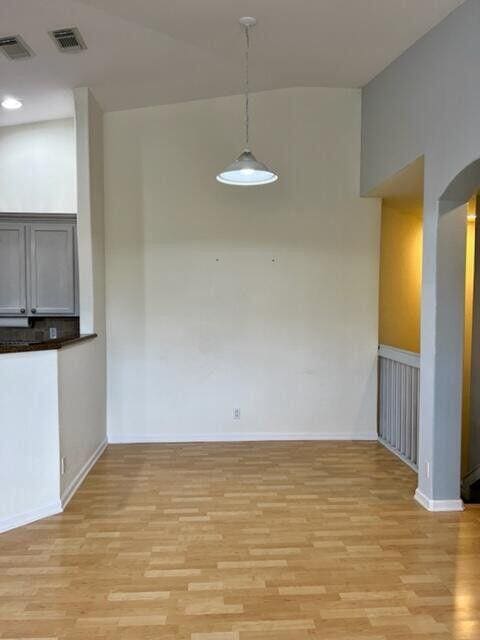 unfurnished dining area with arched walkways, visible vents, and light wood-style floors