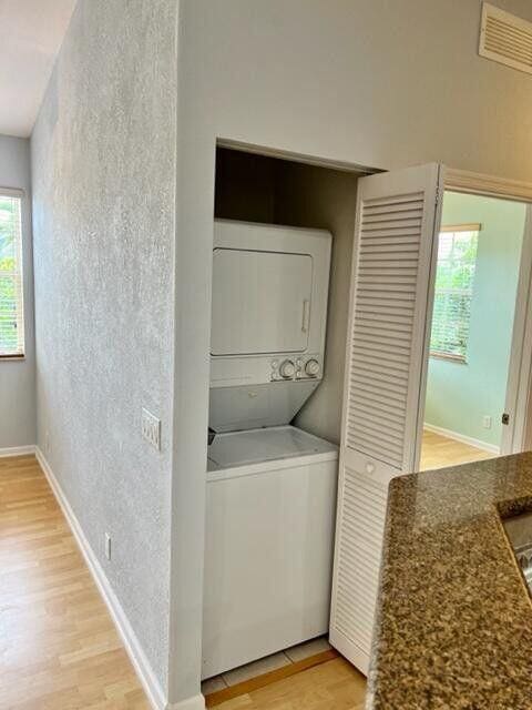 clothes washing area featuring light wood finished floors, stacked washer / drying machine, visible vents, a textured wall, and laundry area