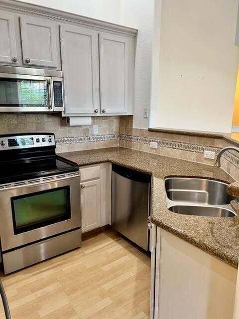 kitchen featuring decorative backsplash, dark stone counters, stainless steel appliances, and a sink