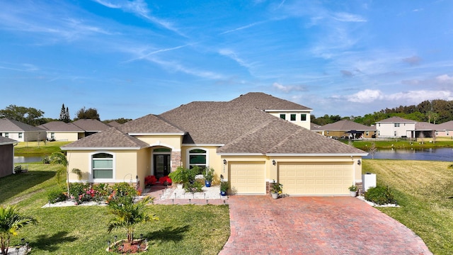 view of front of house featuring decorative driveway, a water view, a front lawn, and stucco siding