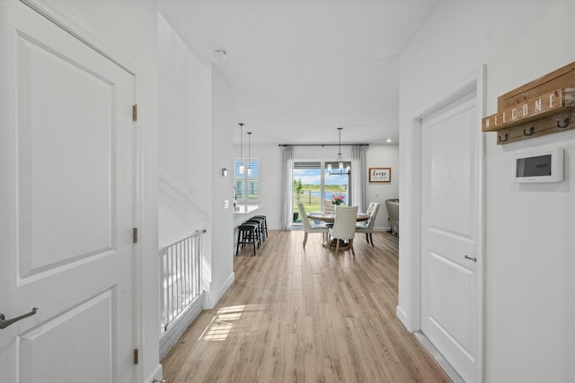 hallway featuring light wood finished floors, baseboards, and a notable chandelier