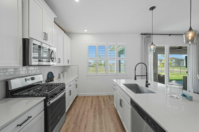 kitchen with a sink, light wood-style floors, light countertops, appliances with stainless steel finishes, and backsplash