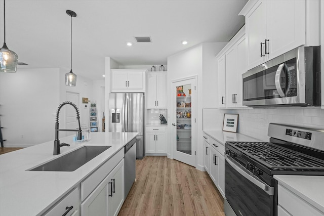 kitchen with light countertops, appliances with stainless steel finishes, hanging light fixtures, and a sink