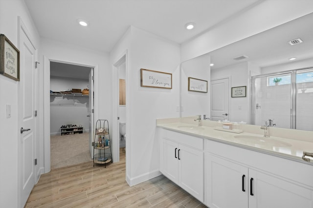 bathroom with visible vents, a sink, a shower stall, and wood finished floors