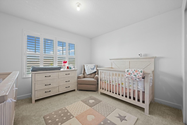 bedroom featuring a nursery area, light colored carpet, and baseboards