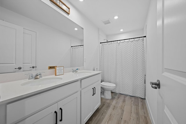 bathroom featuring double vanity, a sink, toilet, and wood finished floors