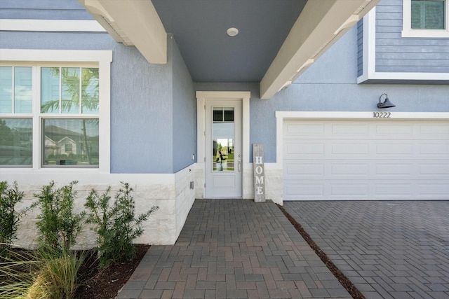 view of exterior entry featuring a garage, decorative driveway, and stucco siding