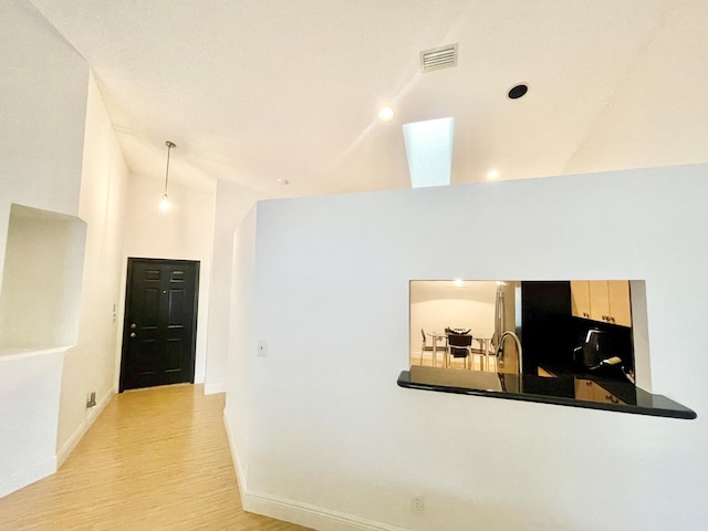 corridor with visible vents, baseboards, vaulted ceiling with skylight, light wood-style flooring, and a sink