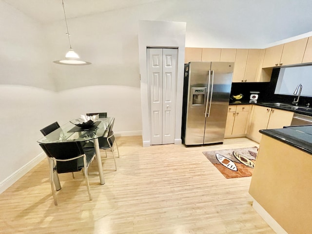 kitchen with light wood finished floors, lofted ceiling, a sink, appliances with stainless steel finishes, and dark countertops