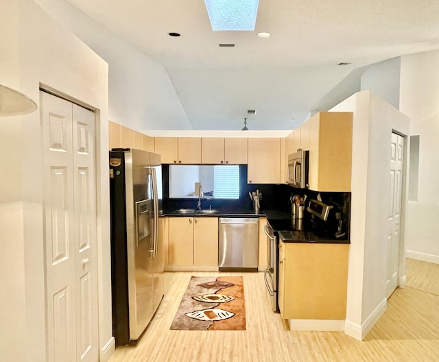 kitchen featuring light wood-type flooring, light brown cabinets, a sink, dark countertops, and appliances with stainless steel finishes