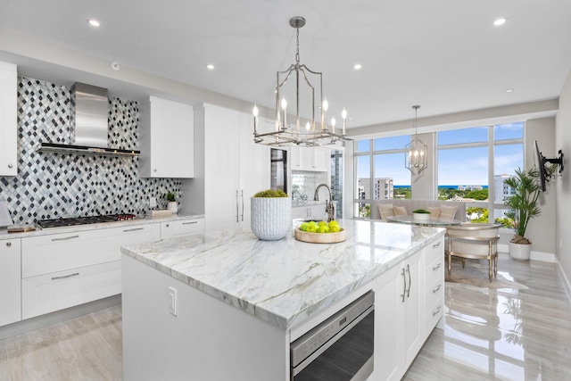 kitchen featuring a chandelier, wall chimney exhaust hood, gas cooktop, and decorative backsplash