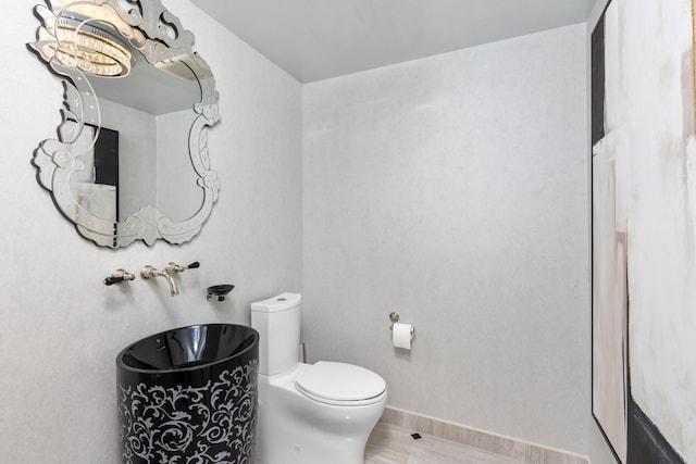 bathroom with an inviting chandelier, toilet, and baseboards