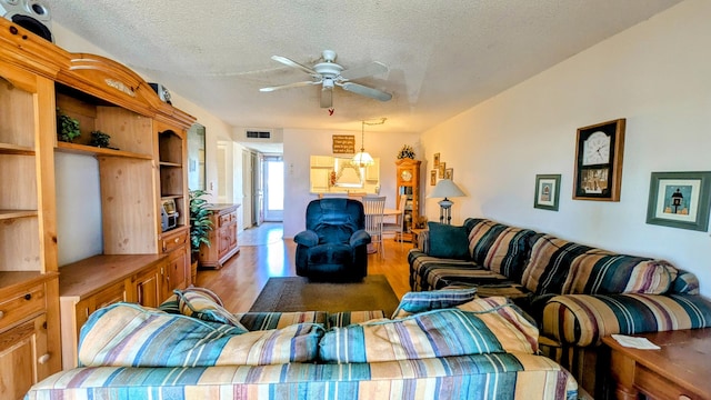 living area with visible vents, ceiling fan, a textured ceiling, and wood finished floors