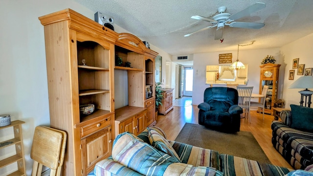 living area featuring a textured ceiling, light wood-type flooring, visible vents, and a ceiling fan