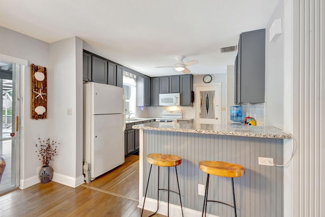 kitchen with a breakfast bar area, a peninsula, white appliances, visible vents, and light wood-type flooring