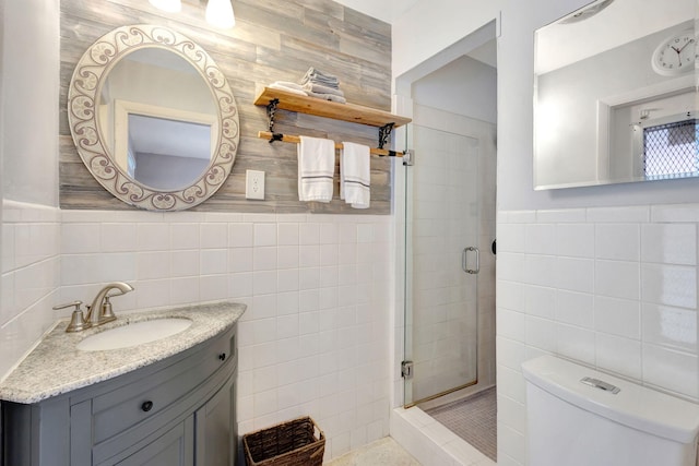 full bathroom featuring a stall shower, wainscoting, toilet, vanity, and tile walls