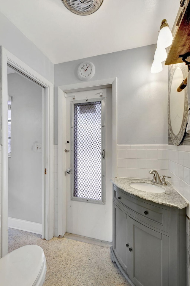 bathroom featuring visible vents, toilet, vanity, speckled floor, and tile walls