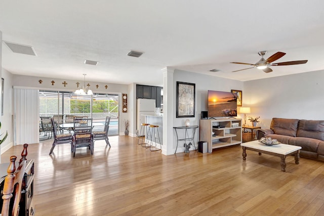 living area featuring light wood-type flooring, visible vents, and ceiling fan with notable chandelier